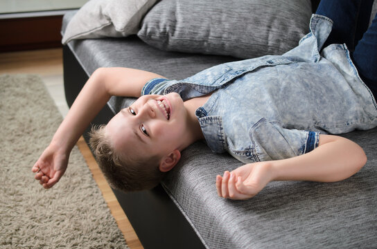 Cute funny boy lying upside down on sofa looking at camera, smiling playful child boy having fun at home.