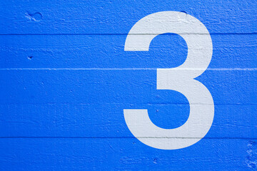 Blue concrete wall with stencil number 3