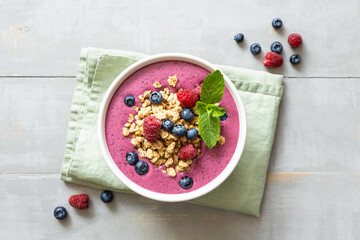 Smoothie bowl with granola and berries decorated with mint on wooden table. Top view.