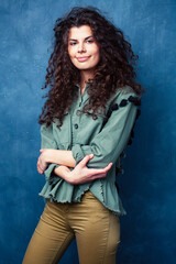 young pretty woman with curly brunette hair posing cheerful on blue background, lifestyle people concept