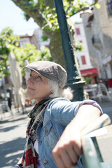 Trendy senior woman with hat relaxing on public bench in small town