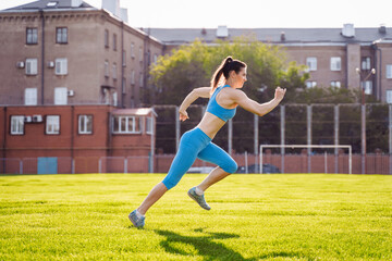 Young professional athlete woman practicing a run on stadium green grass on a sunny morning. Happy with her daily life. Every day increases the speed of her run