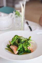 Salmon and green vegetables on a white plate in cafe table with white cloth