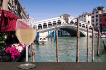 Fototapeta na wymiar Glass of white wine with view on famous Canal Grande and Rialto Bridge in Venice, Italy