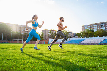 Fototapeta na wymiar Sportsmen man and woman running in stadium. Healthy sport activity for adults. Young athletes in training, runner exercising. Dynamic run of sprinters in a city stadium on the grass