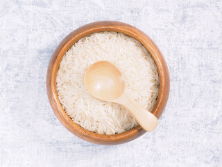Indian long grain Basmati rice in brown wooden bowl and spoon on white concrete background