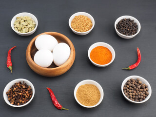 Raw chicken eggs, black pepper, turmeric, masala powder, red chili, cloves, allspice, green cardamom on black wooden background. Ingredients for making scrambled eggs or omelet. Organic food concept