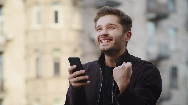 Happy man getting great news phone outside. Overjoyed guy using phone outdoors