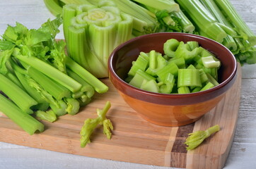 Sliced fresh celery in a clay bowl and Celery stalk on kitchen wooden board