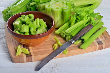 Sliced fresh celery in a clay bowl and Celery stalk on kitchen wooden board