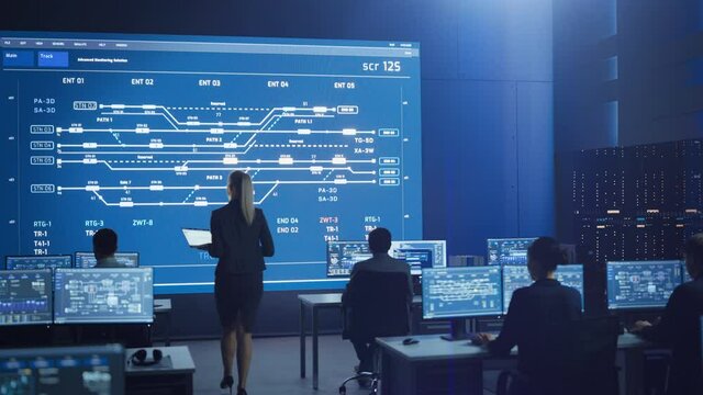 Telecommunications Company System Control and Monitoring Room with Diverse Multicultural Team of Professionals Working on Computers. Big Screen Display Showing Infrastructure Infographics and Data
