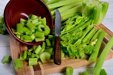 Sliced fresh celery in a clay bowl and Celery stalk on kitchen wooden board