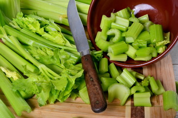 Sliced fresh celery in a clay bowl and Celery stalk on kitchen wooden board