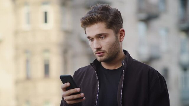 Upset man using phone outside. Annoyed guy looking screen on street.