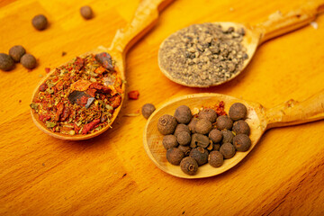 Black allspice, coarse salt and various ground spices in wooden spoons on a wooden Board. Close up.