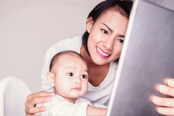 Cute pictures of 2 Asian mothers and son watching their Tablet in the house in a happy mood.