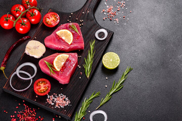 Fresh tuna fillet steaks with spices and herbs on a black background