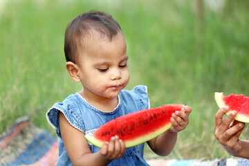 Cute Indian baby girl eating watermelon holding a large peice of melon in her both hands.