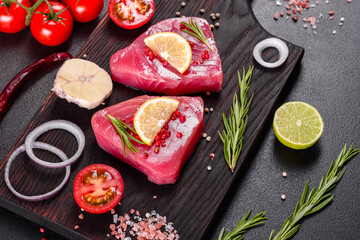 Fresh tuna fillet steaks with spices and herbs on a black background