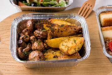 Food Delivery Concept. Container with mushrooms and potatoes on a wooden board