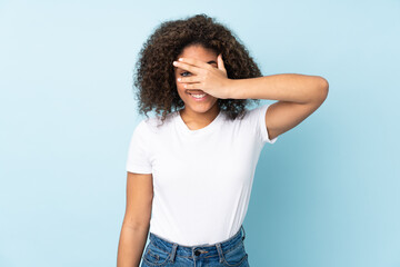 Young African American woman isolated on blue background covering eyes by hands and smiling