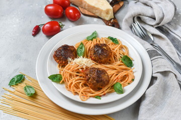 Meatballs in tomato sauce with pasta spaghetti on white plate on light stone table. Top view with copy space.