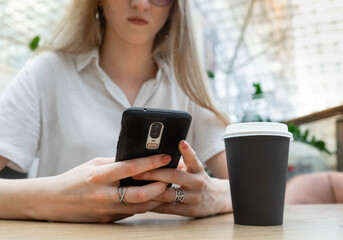 Close up of a smartphone being used by cheerful young caucasian blond business woman in a white shirt sitting at the table. Concept of successful young women on coffe break. Lifestyle concept