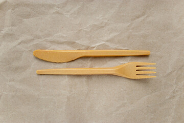 Biodegradable disposable cutlery: fork and knife on crumpled brown craft paper background. Concept of zero waste, eco friendly. Selective focus
