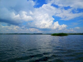 A small island in the middle of a lake under a sky full of air clouds.