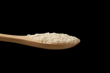 Close up white sesame seeds in wooden spoon on black background.