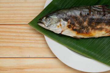 Close up grilled fish placed on banana leaf on a white plate with copy space.