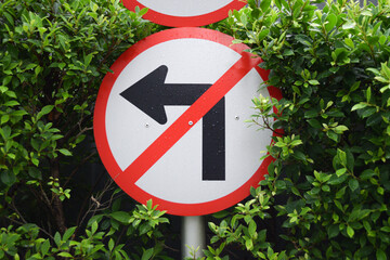 Do not turn left sign warning on shrub background. Round traffic sign plate.