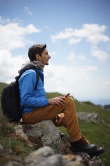 A young male tourist sitting on a rock. He is on the summit of Stara Planina (Balkan Mountains) and enjoying the view. In one of his hands, he's holding a wooden flute/ pipe.