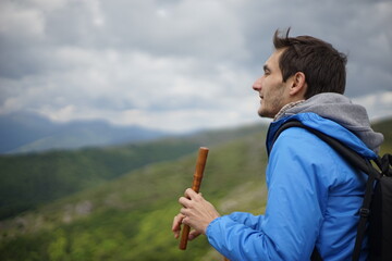 A side view of a young male tourist playing a wooden reed-pipe/ flute. He is on the summit of Stara Planina (Balkan Mountains). 