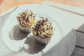 Appetizing cupcakes with white cream decorated with balls of confectionery powder lit by the rays of the sun.