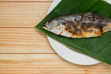 Close up grilled fish placed on banana leaf on a white plate with copy space.