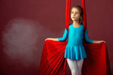 Fearless pretty little girl in a blue gymnastic suit shows a stunt aerial red ribbon surrounded by...