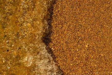 The surface of the sea shore is completely covered with small shells, sea shells and a wave.
