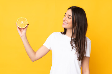 Young caucasian woman holding an orange isolated on yellow background with happy expression