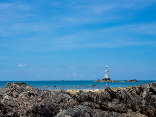 Fototapeta na wymiar Lighthouse in bright sunny summer day in the sea of Thailand. Rocky coast out of focus in the front.