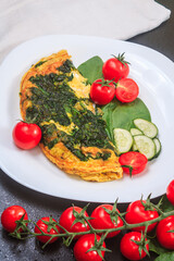 fried eggs with spinach and tomatoes, cucumbers on a white large plate on a black embossed table. copy space, close up. vertical orientation