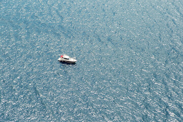 A yacht or a boat floats alone on the big water in sun glare. Open sea without wind.