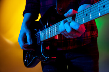 Obraz na płótnie Canvas Close up young inspired and expressive musician, guitarist performing on gradient colored background in neon light. Concept of music, hobby, festival, art. Joyful artist, colorful, bright portrait.