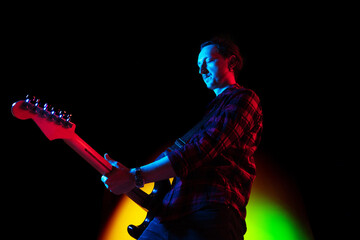 Fototapeta premium Dark mood. Young inspired and expressive musician, guitarist performing on gradient colored background in neon light. Concept of music, hobby, festival, art. Joyful artist, colorful, bright portrait.
