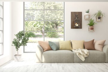 Fototapeta premium White living room with sofa and summer landscape in window. Scandinavian interior design. 3D illustration