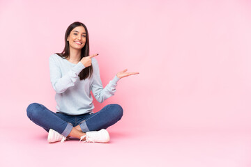 Fototapeta na wymiar Young caucasian woman isolated on pink background holding copyspace imaginary on the palm to insert an ad
