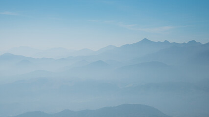 Fototapeta na wymiar Mountain range silhouette in the mist with blue sky background 