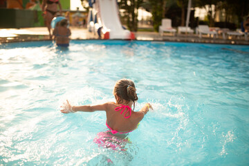 Top view happy little girl in bright color swimwear swims in the clear warm pool water Sunny summer day during vacation. Family vacation and tourism concept. Advertising space