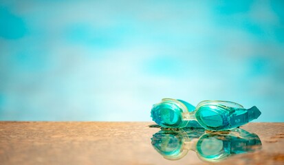 Close-up of waterproof children's swimming goggles lie on a wooden surface against the background of a blurred pool on a warm summer day. Concept of vacation with children at sea. Advertising space