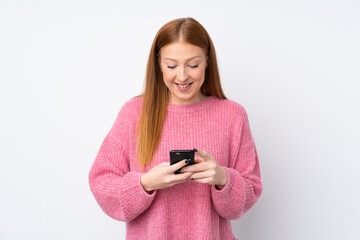 Young redhead woman with pink sweater over isolated white background sending a message with the mobile